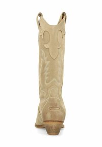 Beige suede cowboylaarzen met een spitse neus, decoratieve stiksels en treklussen. Hakhoogte van ongeveer 5 centimeter.