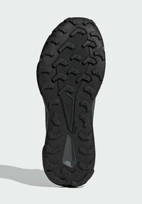 Schwarze Gummisohle mit tiefen Stollen, die ein geometrisches Muster und eine zentrale Aussparung zur Flexibilität aufweist. Entwickelt für Traktion und Langlebigkeit.