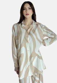 Beige og hvid mønstret silke skjorte med spids krave, lange ærmer og knaplukning, med abstrakte bølge-lignende design.