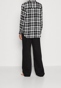 Camicia a scacchi in bianco e nero con maniche lunghe, vestibilità rilassata e orlo curvo, abbinata a pantaloni neri larghi.