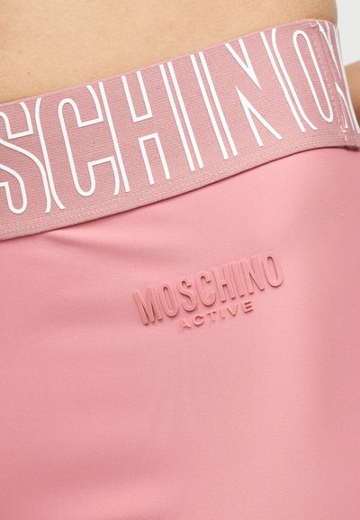 Κοντινό πλάνο σε ροζ κολάν Moschino Active με ελαστική μέση που έχει μεγάλο λευκό γράψιμο Moschino.