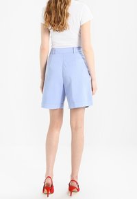 Světle modré bavlněné šortky s rovnými nohavicemi, s olemovaným lemem. V kombinaci s červenými sandály na vysokém podpatku a přiléhavým bílým topem.