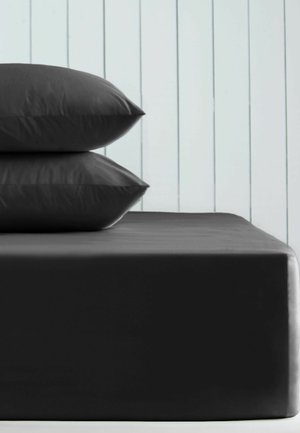 Zwei schwarze Kissen auf einer schwarzen Matratze gestapelt vor einer weißen vertikal getäfelten Wand.