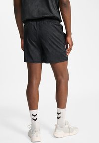 Svarta träningsshorts i texturerat tyg, med elastiskt midjeband, sidofickor och en liten logotyp på vänster lår. Skorna är lätta sneakers och mönstrade strumpor.