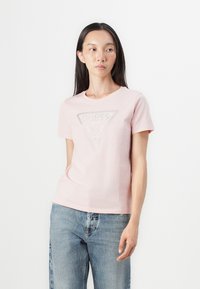 Camiseta de algodón rosa claro de manga corta, con un triángulo del logo GUESS en strass plateados en la parte frontal.