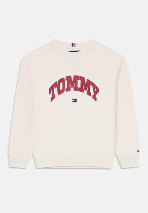 Sweatshirt crème avec le texte rouge "TOMMY", des poignets côtelés, un col arrondi et un petit logo navy, rouge et blanc sur l'ourlet.