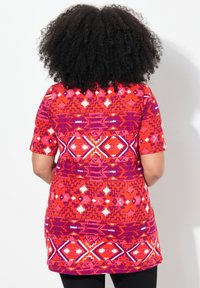 Túnica de colores rojo y púrpura con un patrón que presenta diseños geométricos, de mangas cortas y un corte relajado, fabricada con una tela suave y texturizada.