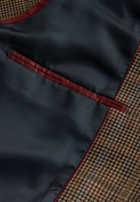 Blue satin fabric with a burgundy trim overlaps a brown houndstooth pattern, featuring a small pocket integrated into the design.