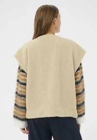 Bež fleece majica s teksturiranim završetkom, kratkim rukavima i dugim prugastim rukavima u smeđoj, crnoj i bijeloj boji. Jednostavan, opušten dizajn.