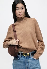 Καφέ πλεκτό πουλόβερ με ψηλό λαιμό και ραφές, συνδυασμένο με ψηλόμεσα ανοιχτό μπλε τζιν και καφέ σουέτ τσάντα ώμου. Χρυσή αγκράφα ζώνης.