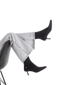 Botas negras de tobillo con punta afilada y un tacón de 5 cm, hechas de material suave. Combinadas con jeans de pierna ancha en gris claro.