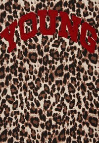 Leopardskinns tyg i brunt och svart, med röda broderade bokstäver som stavar "YOUNG" överst. Mjuk, texturerad yta.