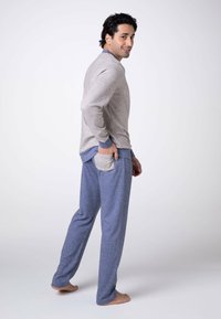 Maglietta grigia a maniche lunghe con dettagli blu, abbinata a pantaloni da pigiama blu con tasca frontale. Tessuto morbido, vestibilità comoda e design casual.