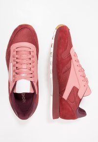 Des baskets de sport rouges et roses comportant des matériaux en mesh et en daim, un design complexe, ainsi qu'une semelle blanche et gomme avec des accents texturés.