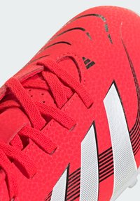 Scarpe da calcio rosse con tomaia sintetica testurizzata, caratterizzate da strisce bianche, dettagli neri e lacci rossi abbinati.