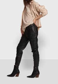 Svarta läder-joggingbyxor med sidfickor, kombinerat med en beige långärmad topp och svarta klackboots vid vristen med träklackar.