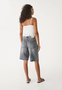 Shorts bermuda en denim gris à coupe décontractée, associés à un crop top blanc smocké avec un ourlet volanté et des fines bretelles.