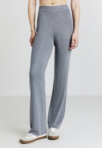 Pantalon large gris clair en tissu tricot doux. Caractérisé par une taille haute élastique et une texture côtelée verticale subtile. Assorti à des baskets blanches.