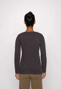 Langärmliges Shirt in Dunkelgrau, aus weichem Stoff, mit rundemHalsausschnitt und leicht lockerer Passform. Trägerin hat die Haare zu einem Dutt gebunden.