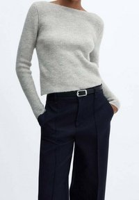 Helle graue Rippenstrickpullover mit langen Ärmeln, kombiniert mit dunkel gestreiften Hosen und einem dünnen schwarzen Gürtel mit einer silbernen Schnalle.