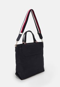 Borsa tote nera realizzata in materiale resistente, con tasca frontale, manici doppi e una tracolla regolabile a righe rossa, bianca e blu.