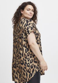 Topp i leopardmönster i tan och svart, kort ärm, avslappnad passform, flödande tyg, rundad nederkant med sidoflikar, subtil lyster.