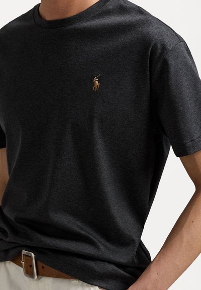 Tmavohnedé bavlnené tričko s okrúhlym výstrihom. Na ľavej strane hrude má malé vyšívané logo polo. Má mäkkú štruktúru a krátke rukávy.