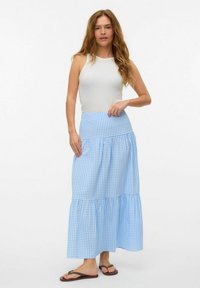 Blå och vit rutigt, lager-på-lager maxi kjol gjord av lättviktsmaterial, parat med en vit linne och flip-flops.