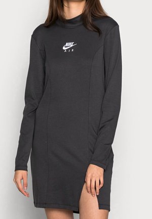 Czarna sukienka Nike Air z długim rękawem, okrągłym dekoltem i rozcięciem na przednim udzie, noszona przez osobę o długich brązowych włosach.