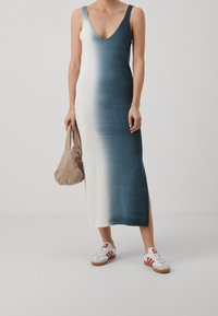 Robe longue sans manches à col en V avec un dégradé allant du bleu profond au blanc. Assortie à des baskets blanches et un sac à main beige.