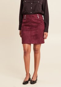 Bordeaux suède mini-rok met een getailleerde vorm, voorzien van decoratieve zilveren knopen aan de voorkant als accentdetail.