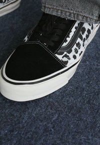 Sorte semsket og hvit tekstil sneakers med et leopardmønster, svarte snøringer og en tykk hvit gummisåle.