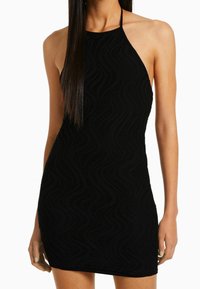 Robe noire à bretelles avec motif en vagues texturé, silhouette moulante et design minimaliste. Bretelles ajustables et longueur courte.