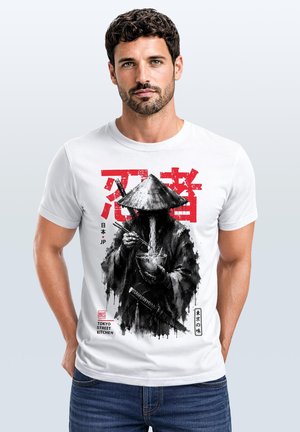 Mann trägt weißes T-Shirt mit schwarzer und roter Grafik eines Ninjas, der mit Essstäbchen Nudeln isst und ein Schwert am Gürtel hat.