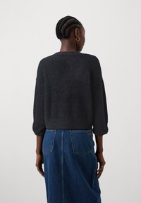 Črna, puhasta pulover s tremi četrtinskimi rokavi; oblečena z denim krilom, ki ima dve zadnji žepki in rahel razširitev.