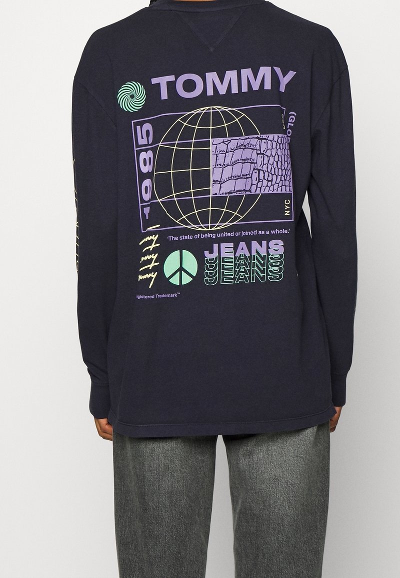 Svart långärmad skjorta med grafiska mönster i lila och grönt, inklusive en glob, textelement och mönster. Avslappnad passform med ribbade ärmslut.