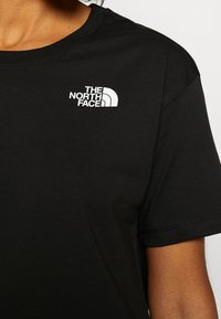 Svart kortärmad T-shirt i bomull med en vit logotyp på vänster bröst. Enkel rund halsringning och sydda ärmkanter.