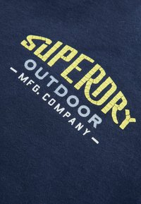 Marinblå sweatshirt med texturerade gult och vitt tryck "Superdry Outdoor Mfg. Company" på ett mjukt tyg.