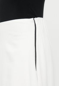 Jupe blanche avec un détail de passepoil noir sur le côté, présentée sur un torse de mannequin noir devant un fond uni.
