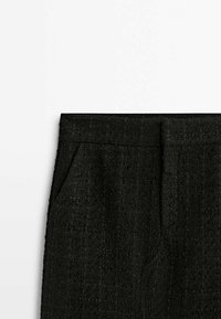 Pantalons noirs texturés avec une taille plate et des poches latérales. Le matériau ressemble à un tissu tissé avec un motif subtil.
