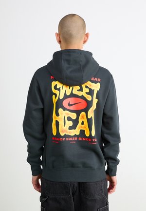 Felpa grigia con cappuccio caratterizzata da una grafica audace gialla con la scritta "SWEET HEAT" e accenti rossi, insieme al logo Nike; texture morbida e vestibilità comoda.