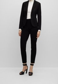 Mustavärinen räätälöity bleiseri, jossa on kaksi nappia, yhdistettynä slim-fit mustiin housuihin ja mustiin korkokenkiin, joissa on nilkkaremmistit.