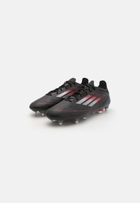 Black football boots with a textured upper, featuring red and white stripes, lace closure, and six metal studs for traction.