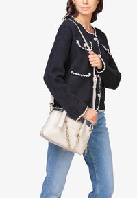 Marineblauwe gestructureerde jas met witte afwerking en knopen, gecombineerd met een kleine crèmekleurige handtas met kettingdetail, gedragen met lichtblauwe jeans.