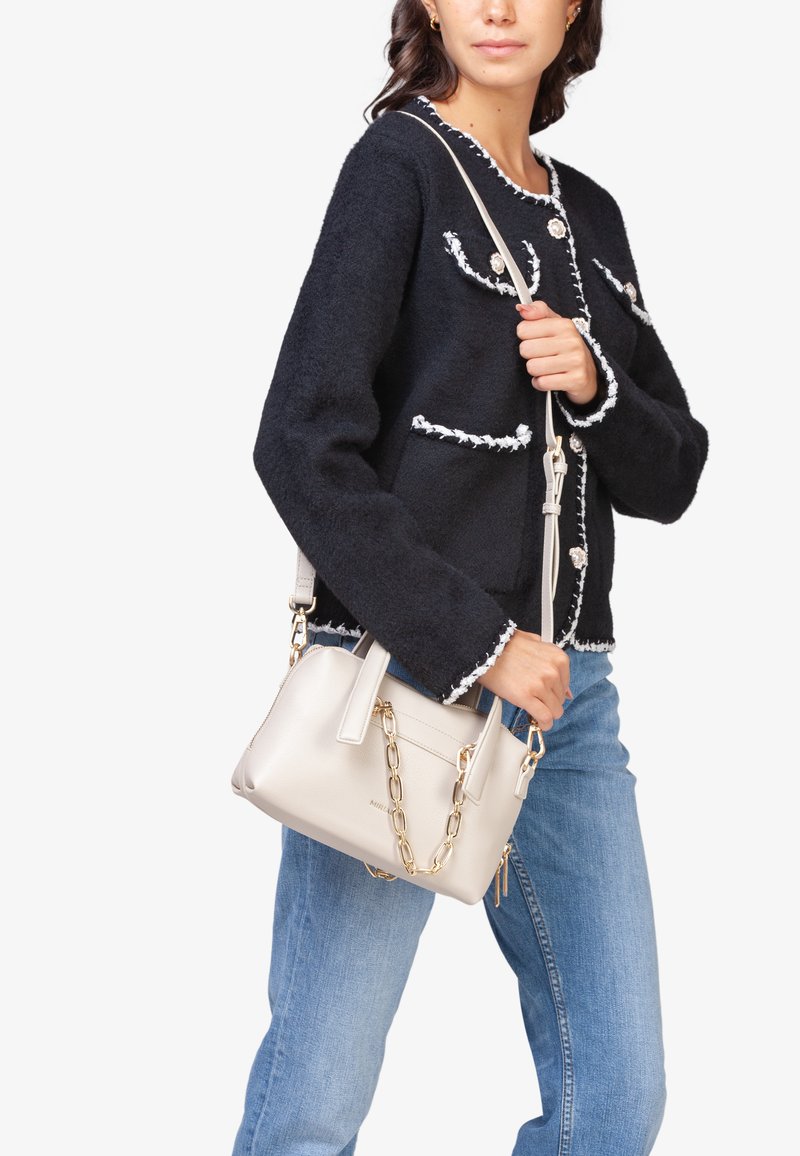 Marineblauwe gestructureerde jas met witte afwerking en knopen, gecombineerd met een kleine crèmekleurige handtas met kettingdetail, gedragen met lichtblauwe jeans.