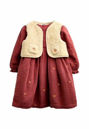 Vestito rosso a maniche lunghe con piccoli fiori ricamati abbinato a un gilet sherpa senza maniche color crema con tasche frontali.