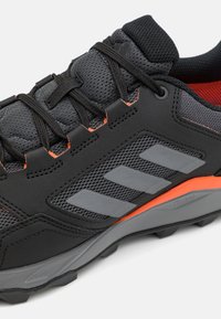 Basket noir avec tige en maille texturée, accents orange, rayures grises sur le côté, et une semelle en caoutchouc durable avec un motif de traction.