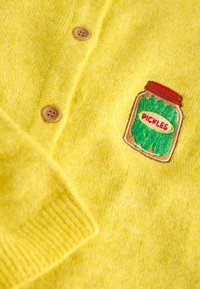 Keltainen neuletakki, jossa puiset napit ja suolakurkkujen purkki - kirjailu. Kangas on pehmeää ja siinä on hentoinen kuvio.