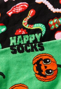 Chaussettes colorées avec une base noire ornée de motifs de fruits de mer et une section verte affichant des citrouilles souriantes, avec "HAPPY SOCKS" en gras noir.