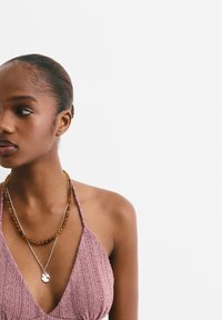 Halter top v texturované světle růžové látce, doplněný o dvě náhrdelníky: jeden s jantarovými korálky a stříbrným přívěskem na řetízku.